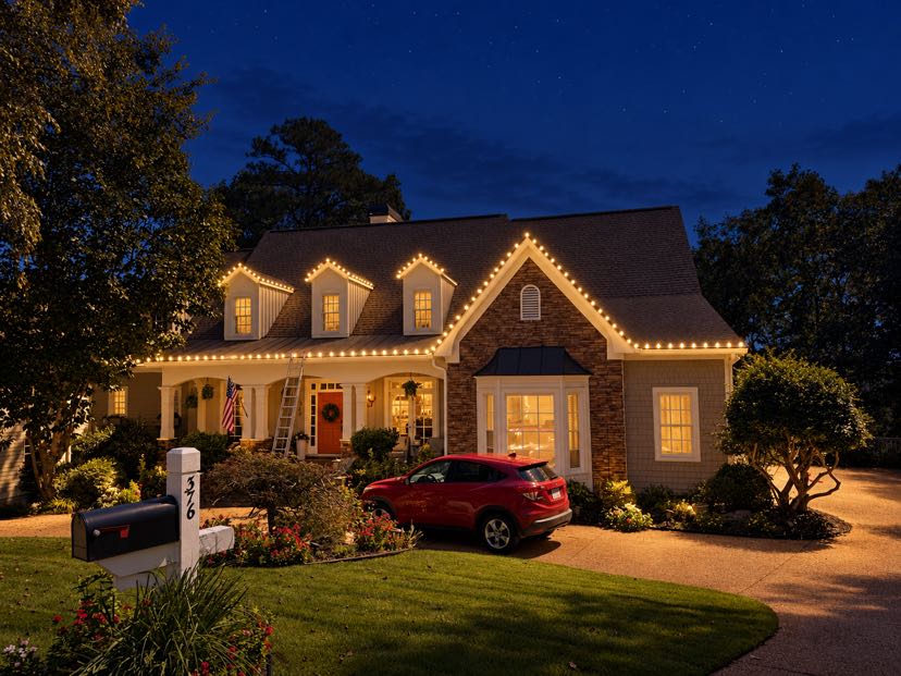 Illuminated two-story home with brick exterior and red SUV in driveway at dusk