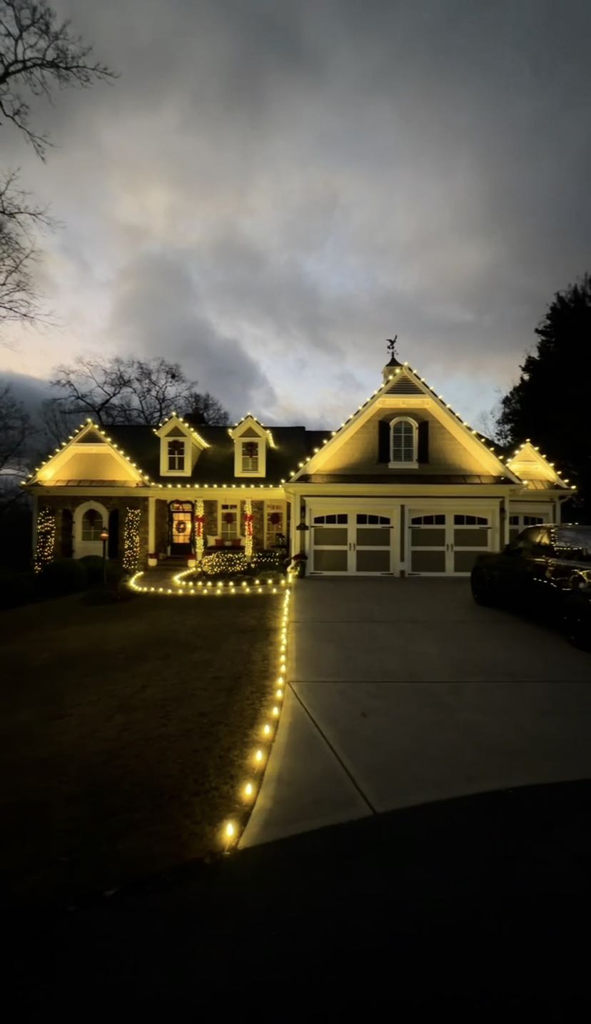 Elegant cream-colored house with warm white string lights outlining driveway and architectural features at dusk