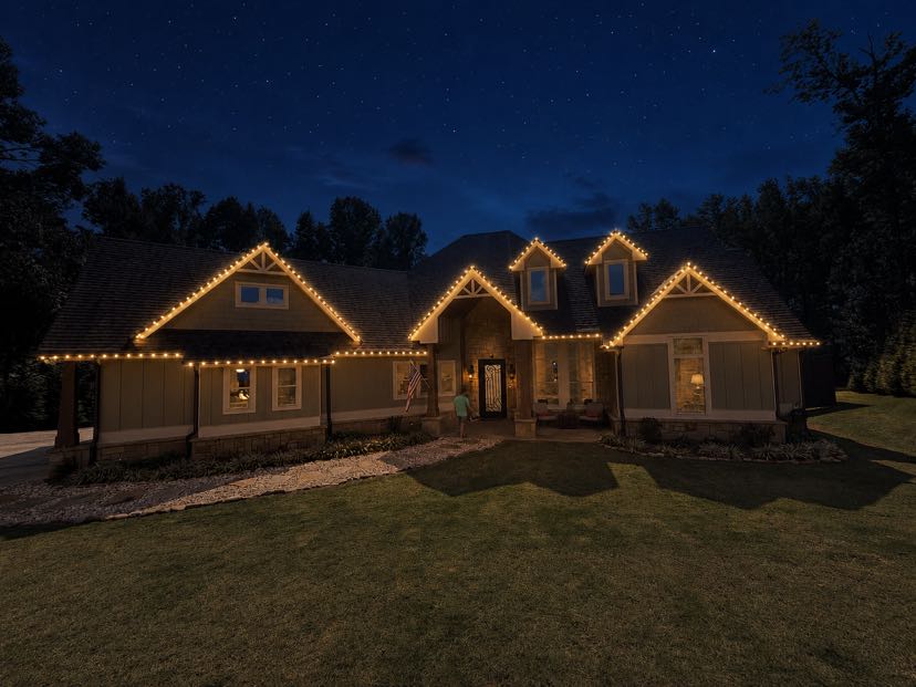 Elegant two-story home illuminated with warm outline lighting at dusk under starry sky